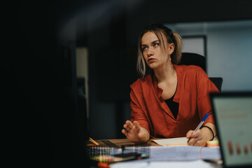 Fototapeta premium A thoughtful businesswoman engaged in intense brainstorming and idea development at a conference table during a late evening meeting, highlighting determination and focus in professional settings.