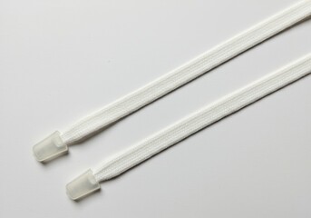 A close up view of two white drawstrings with clear plastic tips on a white surface diagonally