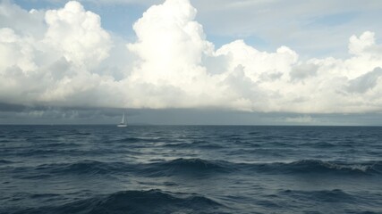 Obraz premium A lone sailboat navigates the vast ocean under a dramatic sky filled with fluffy cumulus clouds and hints of an approaching storm.
