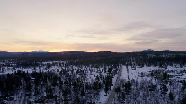 Snow-lined road in Ringebu forest and mountain peaks under twilight sky Norway