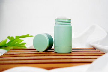 turquoise cylinder skincare packaging with the lid open on wooden pedestal and white fabric as decoration on white background