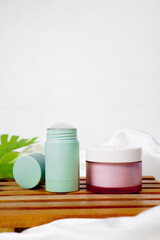 turquoise cylinder skincare packaging with the lid open and magenta skincare jar packaging on wooden pedestal and white background