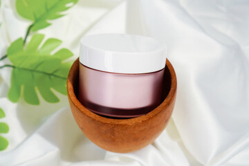 magenta skincare jar packaging in a wooden bowl with white fabric as a base