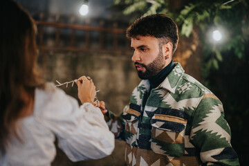 Two individuals arrange string decorations outdoors, with a warm and festive ambiance set by nearby...