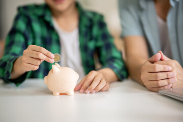 A father is teaching his son how to save money by putting money in a piggy bank.
