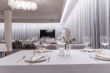 beautiful table decoration in restaurant. festive table setting in restaurant. white tablecloth on table, wine glasses, white plates, flowers in vase, candles are burning. romantic atmosphere