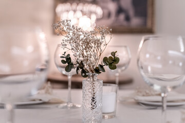 beautiful table decoration in restaurant. festive table setting in restaurant. white tablecloth on table, wine glasses, white plates, flowers in vase, candles are burning. romantic atmosphere