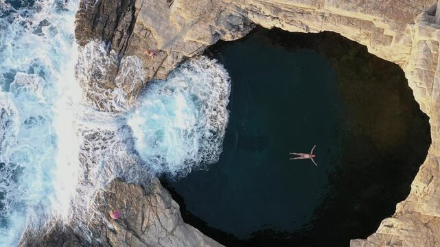  Above aerial slow motion view of a girl floating and swimming in Giola lagoon, natural pool near the sea, in Thassos island, Greece