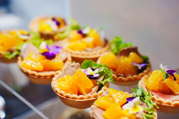 Vibrant fruit tarts with orange and floral garnishes on display