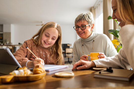 Girl doing homework on a tabletwith mother and grandmother assising
