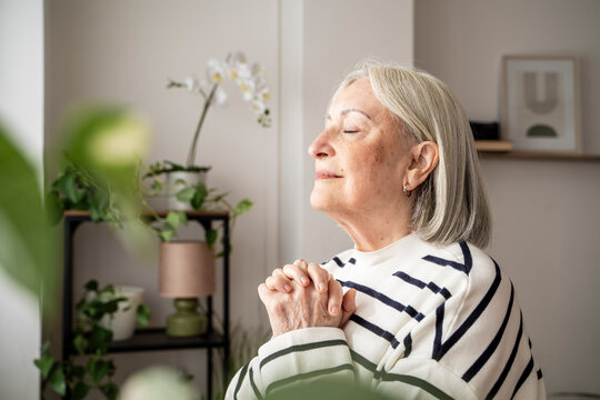 Elderly woman meditating peacefully at home with eyes closed