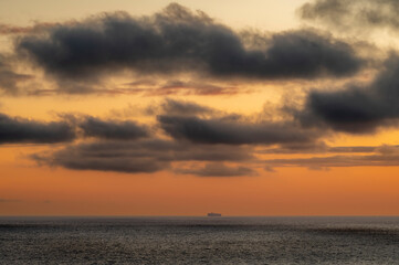 Very moody and dramatic sky over the cloudy ocean horizon, with strong orange, sunbeams and traces of lingering storm cells 