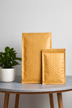 Three bubble mailers mockup on gray desk with office accessories, showcasing yellow and white padded envelopes