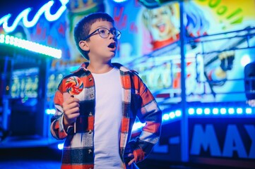 Fototapeta premium A cute Caucasian boy, a child, came to the amusement park to have fun, play and ride a merry-go-round. A child standing in front of a merry go round