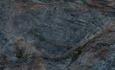 Close-up view of rough, dark gray and reddish rock surface with varied textures and patterns