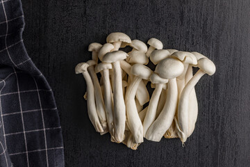 Raw white shimeji mushrooms on black table. Top view.