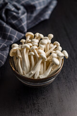Raw white shimeji mushrooms in bowl on black table.