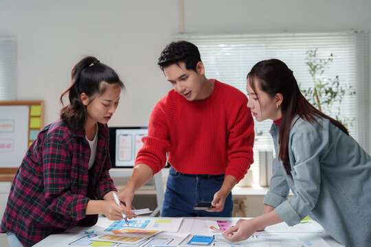 Web designers and programmers working together in a modern office, discussing and planning the design and layout of a mobile application, using wireframes and prototypes