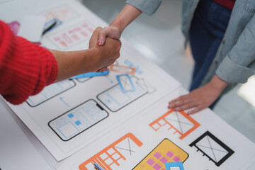 Two ux designers shaking hands after successfully designing a mobile application interface, celebrating their teamwork and achievement in a collaborative workspace