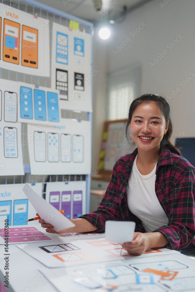 Wall mural smiling asian woman working as a ux ui designer in her office, creating a mobile application interfa
