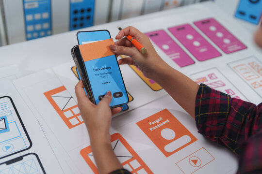 Web designer testing an application prototype on a smartphone while taking notes during the user experience design process for a mobile app, focusing on usability and interface design