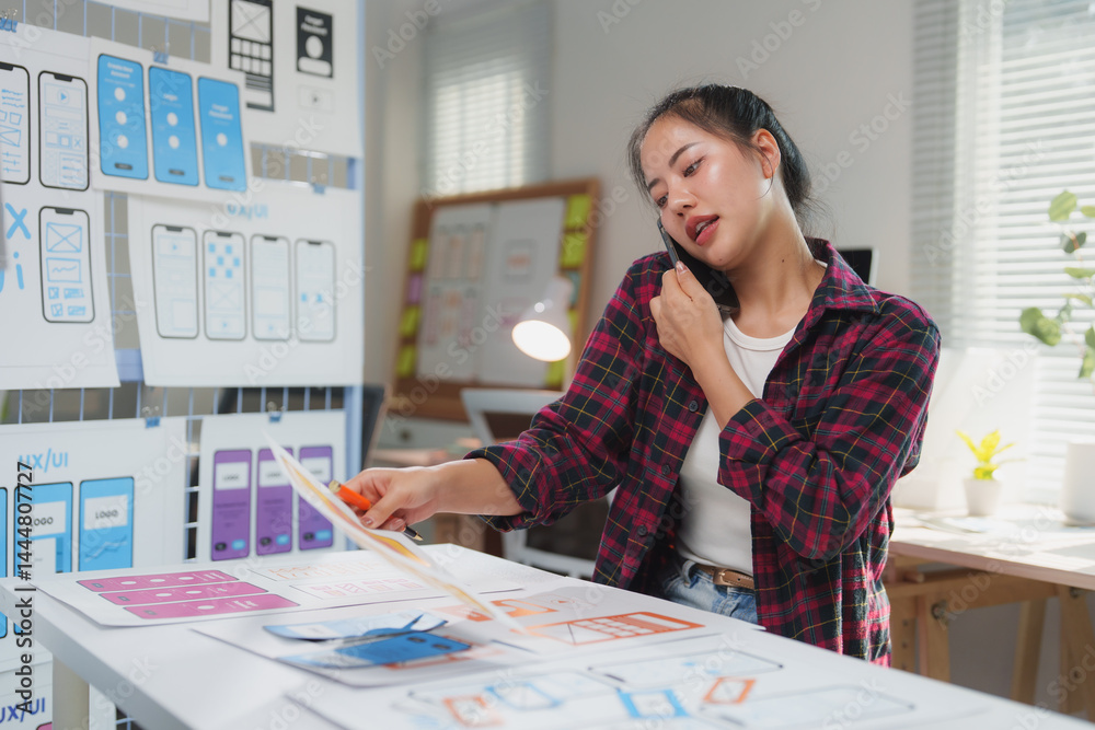 Wall mural female web designer reviewing mobile application wireframes while discussing project details on a ph