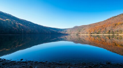 A lake sits in the mountains. The water reflects the mountain scenery. You can see a blue sky above the lake.
