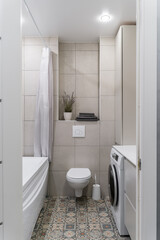 bathroom with light tiles, white bathtub, white toilet, washing machine.