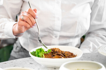 A close-up of a hand holding a fork, enjoying a plated dish featuring tender meat, rice, and fresh greens, elegantly presented on a marble dining table.