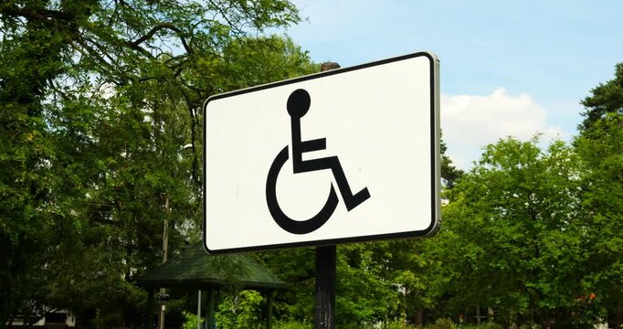 Sign with international symbol of access depicting person in wheelchair near green trees and sky. Sign signifies accessibility for people with disabilities