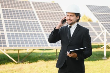 Caucasian engineer using smartphone while standing with solar panel at the background. Concept of...