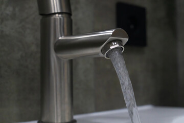 Fresh, clean water flowing from a brushed nickel bathroom faucet into a white sink, complementing a...