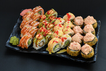 Assorted sushi rolls beautifully arranged on one plate over a black background. Elegant Japanese cuisine set, ideal for restaurant menu or premium food presentation.