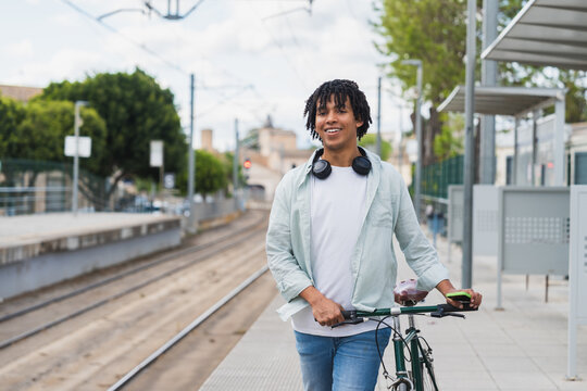 Young African American Man with Bike at Train Station - Smiling young man standing with bicycle at an urban train platform, enjoying a relaxed commute - sustainable mobility and eco-friendly transport - Powered by Adobe