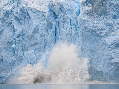 Massive ice chunk breaking off glacier and crashing into Arctic sea during dramatic calving event in Greenland