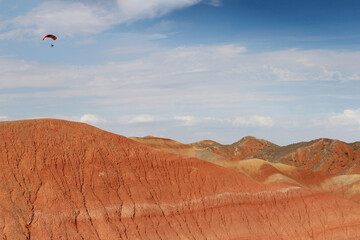 A paraglider flying against the blue sky with white clouds at Zhangye Danxia National Geopark (Rainbow Mountains) in Gansu, China