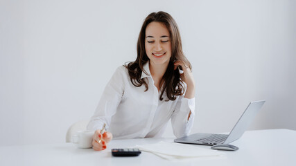 Young woman engaged in work at a bright desk while using a laptop and writing notes in a modern office setting