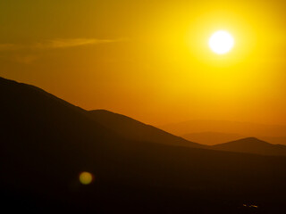 Obraz premium Summer sunset over Pirin Mountains silhouette, Bulgaria, captured from aerial perspective, showcasing layered ridge silhouettes, golden hues, and calm alpine wilderness. Orange sun disk