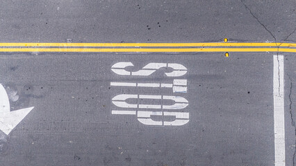 Minimalist top-down drone shot of a grey asphalt road in Long Beach, California, featuring a visible STOP road marking and yellow divider lines.