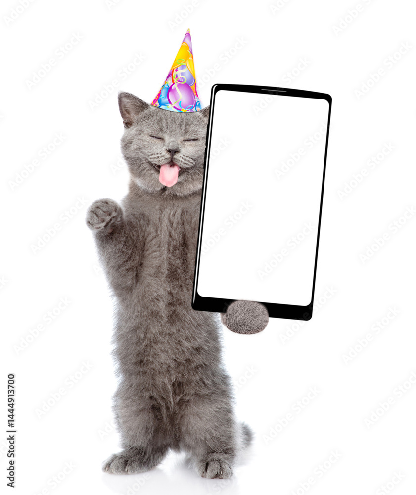 Aufkleber Happy cat with tongiye out wearing party cap standing on hind legs and shows big smartphone with blank screen. Empty space for text. isolated on white background