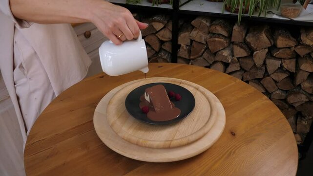 A close-up of the cook pouring liquid chocolate on a cake on a plate in a cafe before serving.
