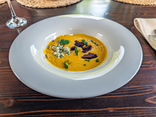 Gourmet Corn Soup with Blue Cheese, Roasted Beetroot, and Herbs in White Bowl.Creamy Yellow Corn Soup Served with Blue Cheese Crumbles and Beet Garnish on Wooden Table