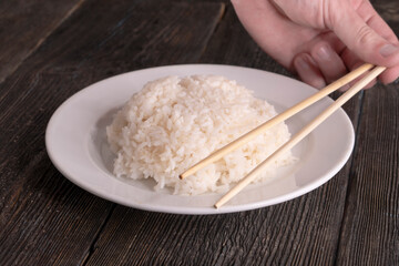 Plate with white rice on black background. Chopsticks