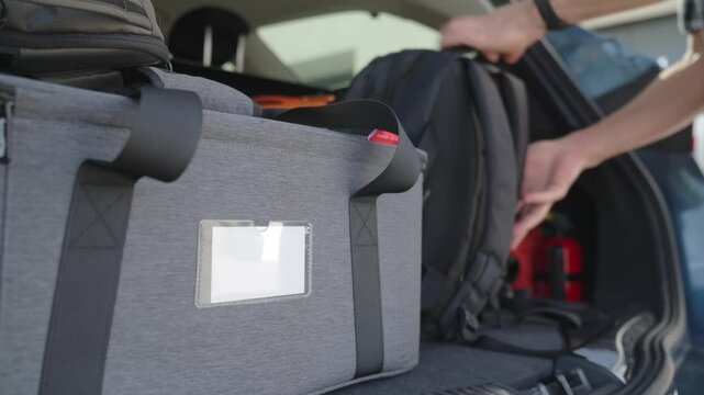 Man loading orange suitcase into car trunk before journey. Packing luggage for travel