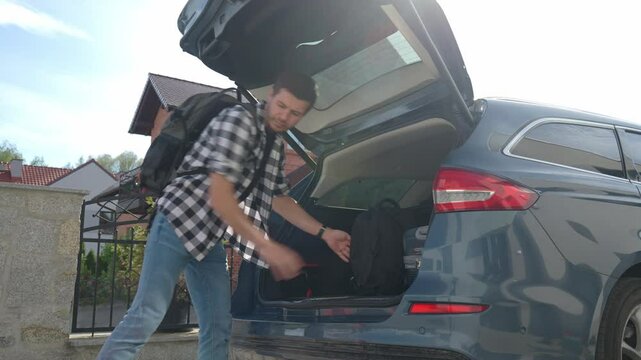 Man loading orange suitcase into car trunk before journey. Packing luggage for travel