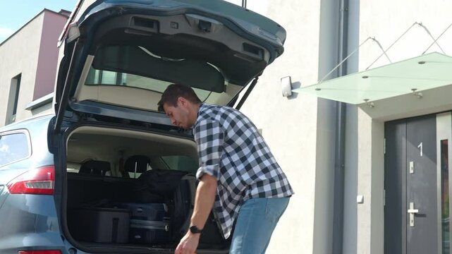 Man loading orange suitcase into car trunk before journey. Packing luggage for travel