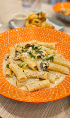 Mushroom penne pasta with cream truffle sauce serving on bright orange plate