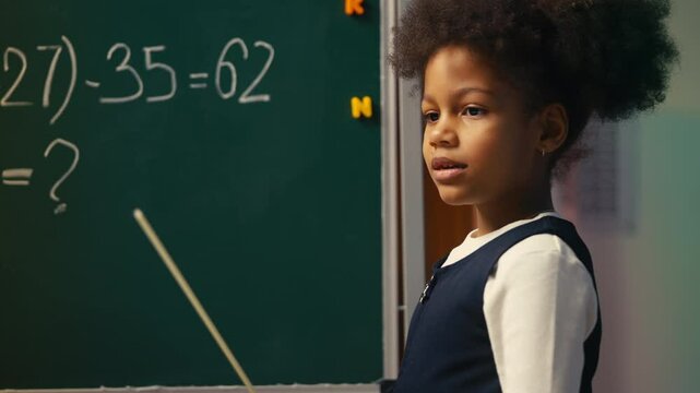African American girl pretending to be math teacher, pointing at chalkboard