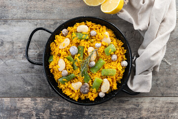 Traditional Valencian paella with rabbit, chicken, garrofon beans, snails, Moroccan green beans and saffron on wooden table