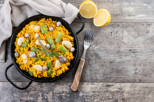Traditional Valencian paella with rabbit, chicken, garrofon beans, snails, Moroccan green beans and saffron on wooden table. Top view. Copy space